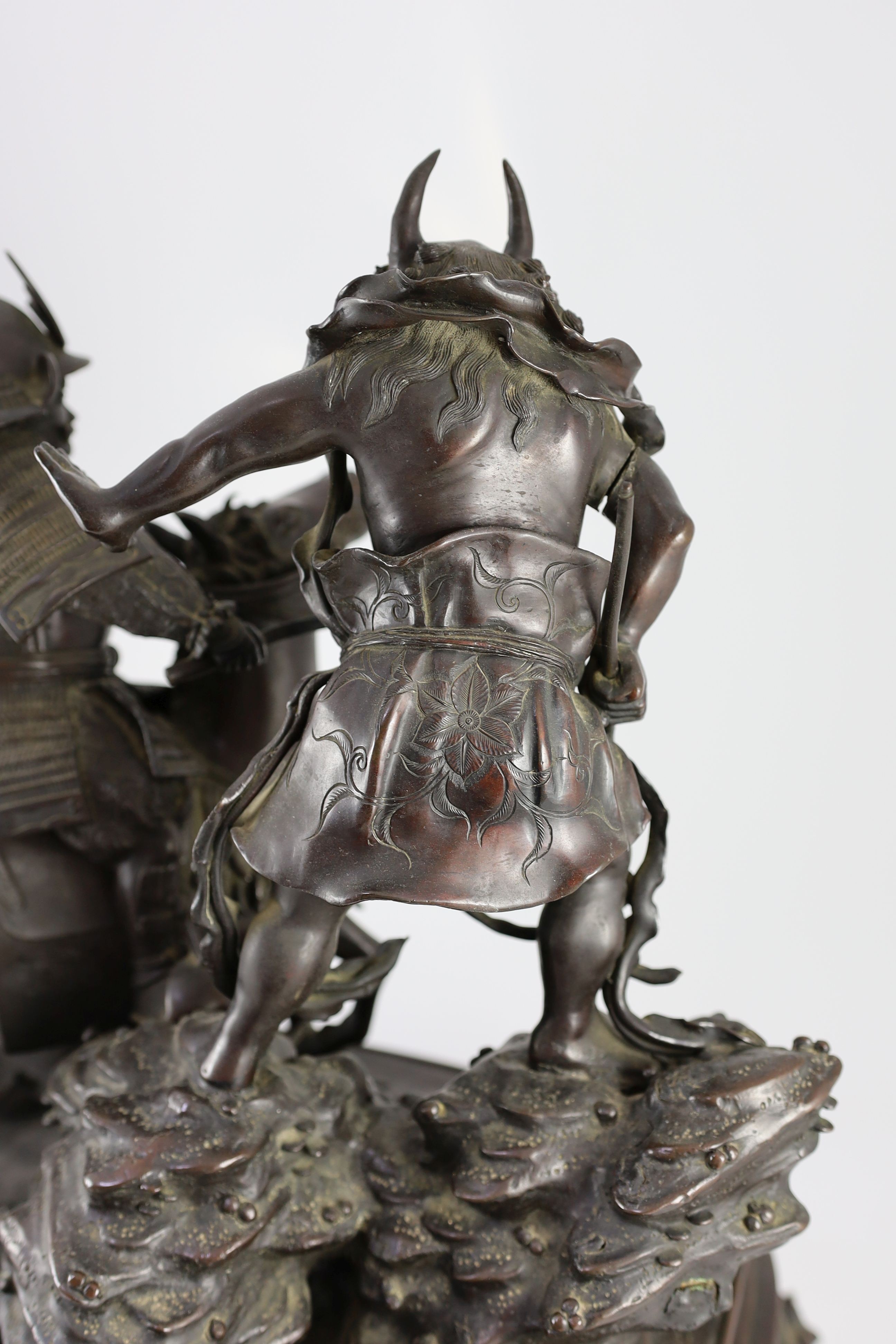 An impressive Japanese bronze group of an oni attacking a Samurai on horseback, Meiji period, 58cm high 49.5cm wide